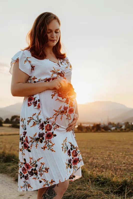Schwangere mit Babyschuhen im Sonnenuntergang – Babybauchfotos im Freien