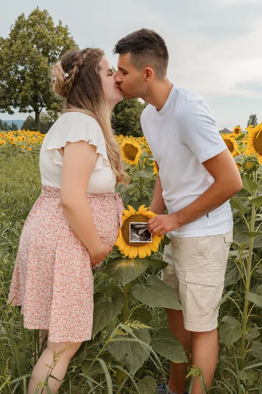 Kuss im Sonnenblumenfeld mit Ultraschallbild – Babybauchshooting, Bezirk Neunkirchen