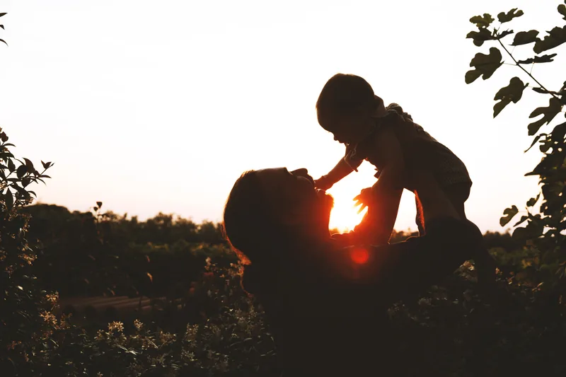 Silhouette: Mutter hebt ihr Kind in den Sonnenuntergang – Familienshooting im Freien